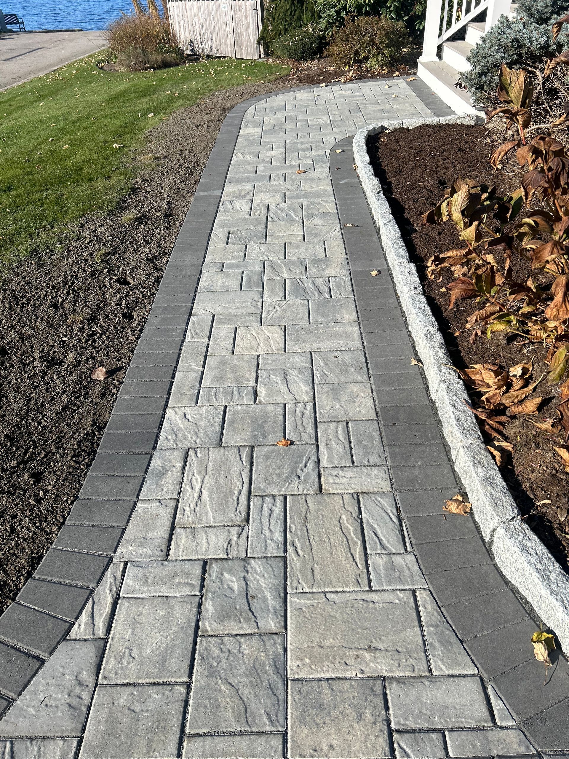A brick walkway leading to a house with a fence in the background.