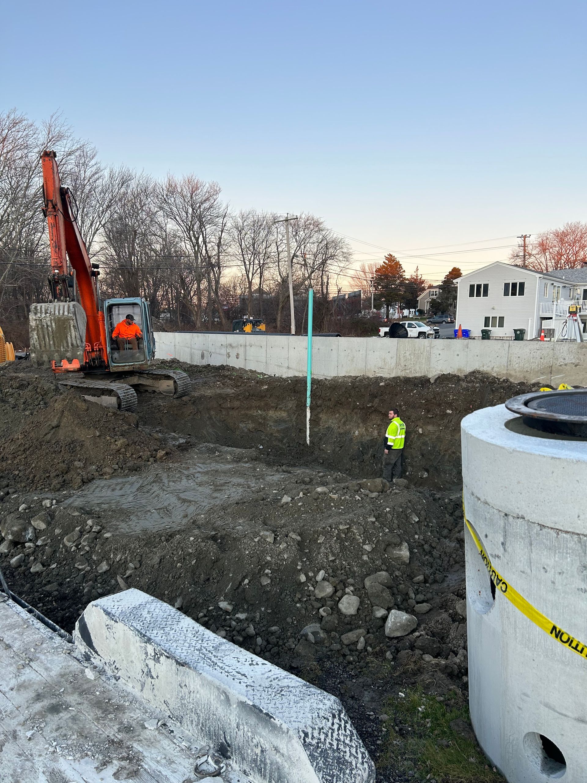 A construction site with a man in a yellow vest standing next to a large concrete cylinder.