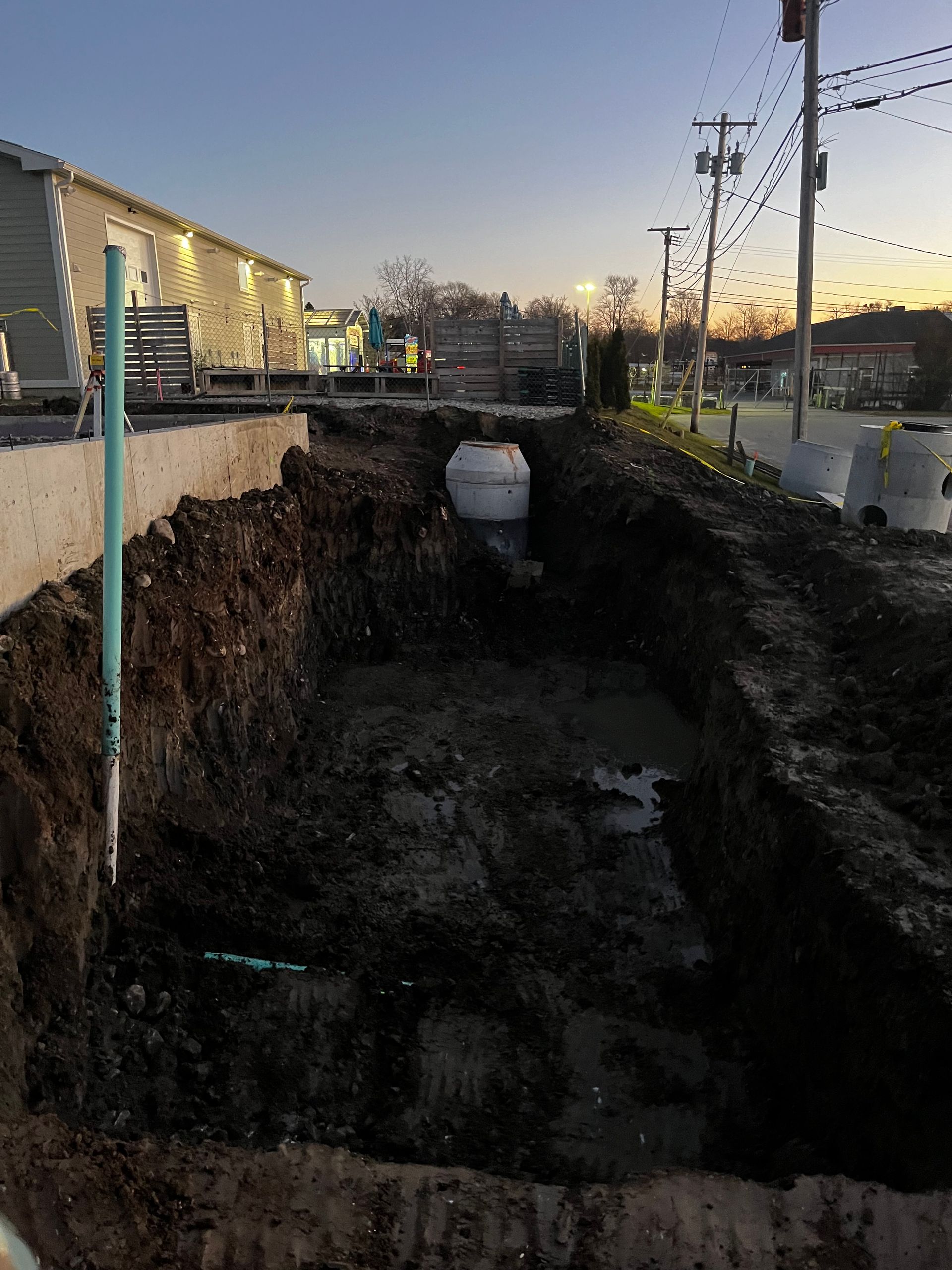 A large hole in the ground next to a road with a building in the background.