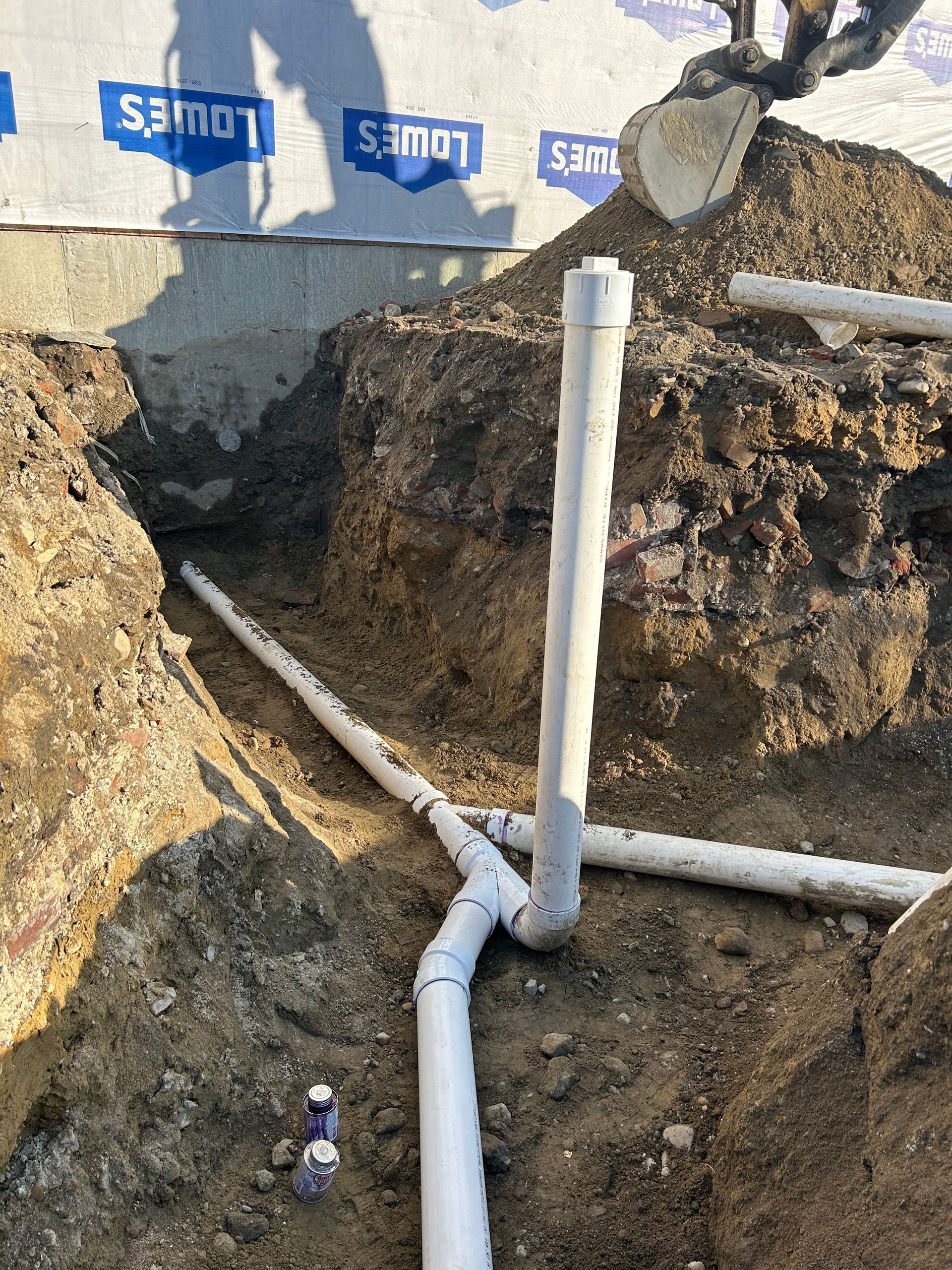 A bunch of pipes are laying in the dirt in a hole.