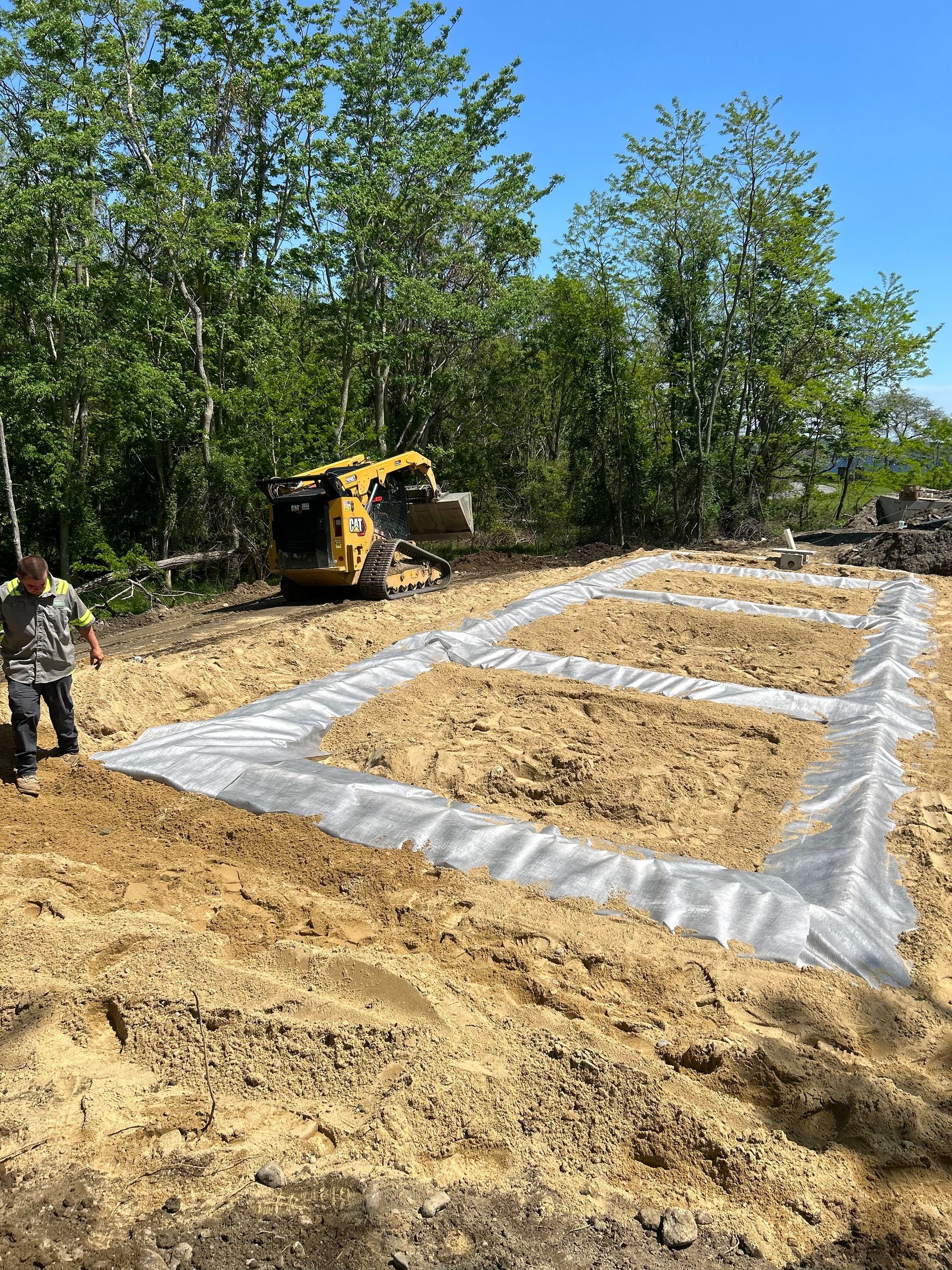 A man is standing in a dirt field with a bulldozer in the background.
