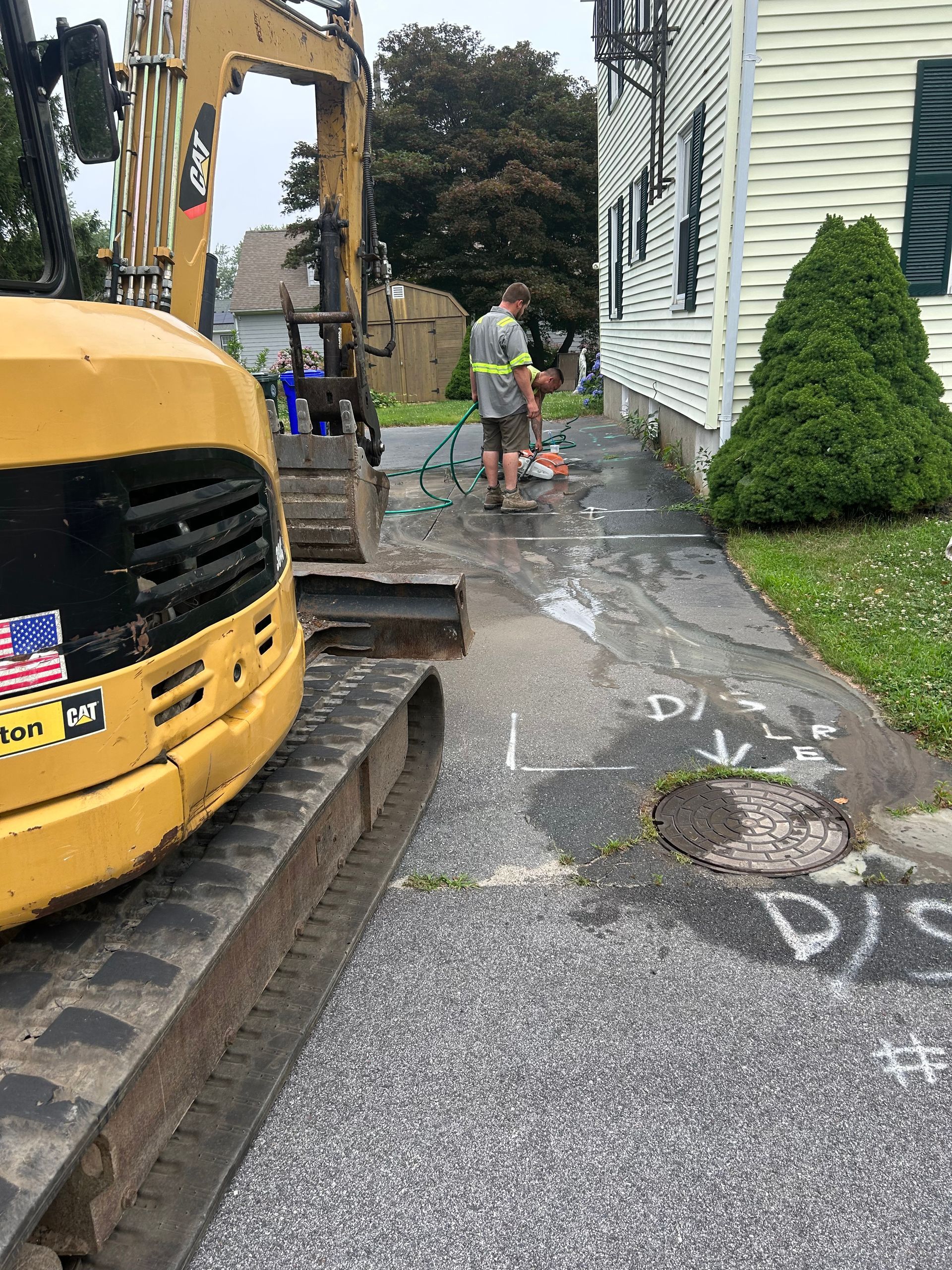 A man is standing next to a yellow excavator in front of a house.