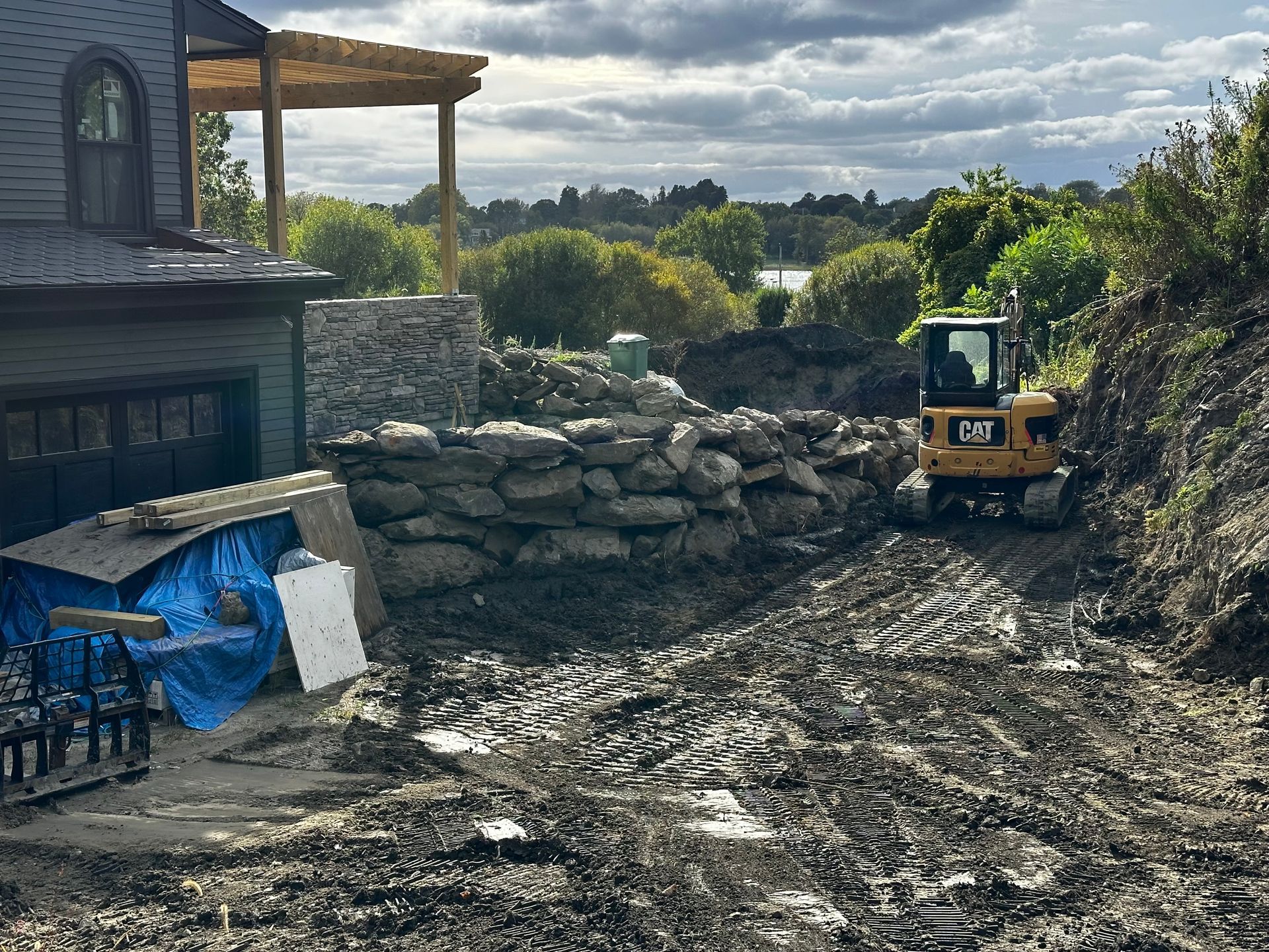 A bulldozer is driving through a muddy field in front of a house.