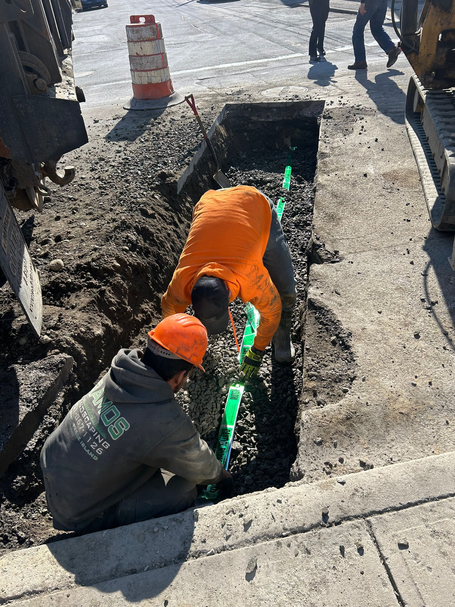Two construction workers are working on a pipe in the ground.
