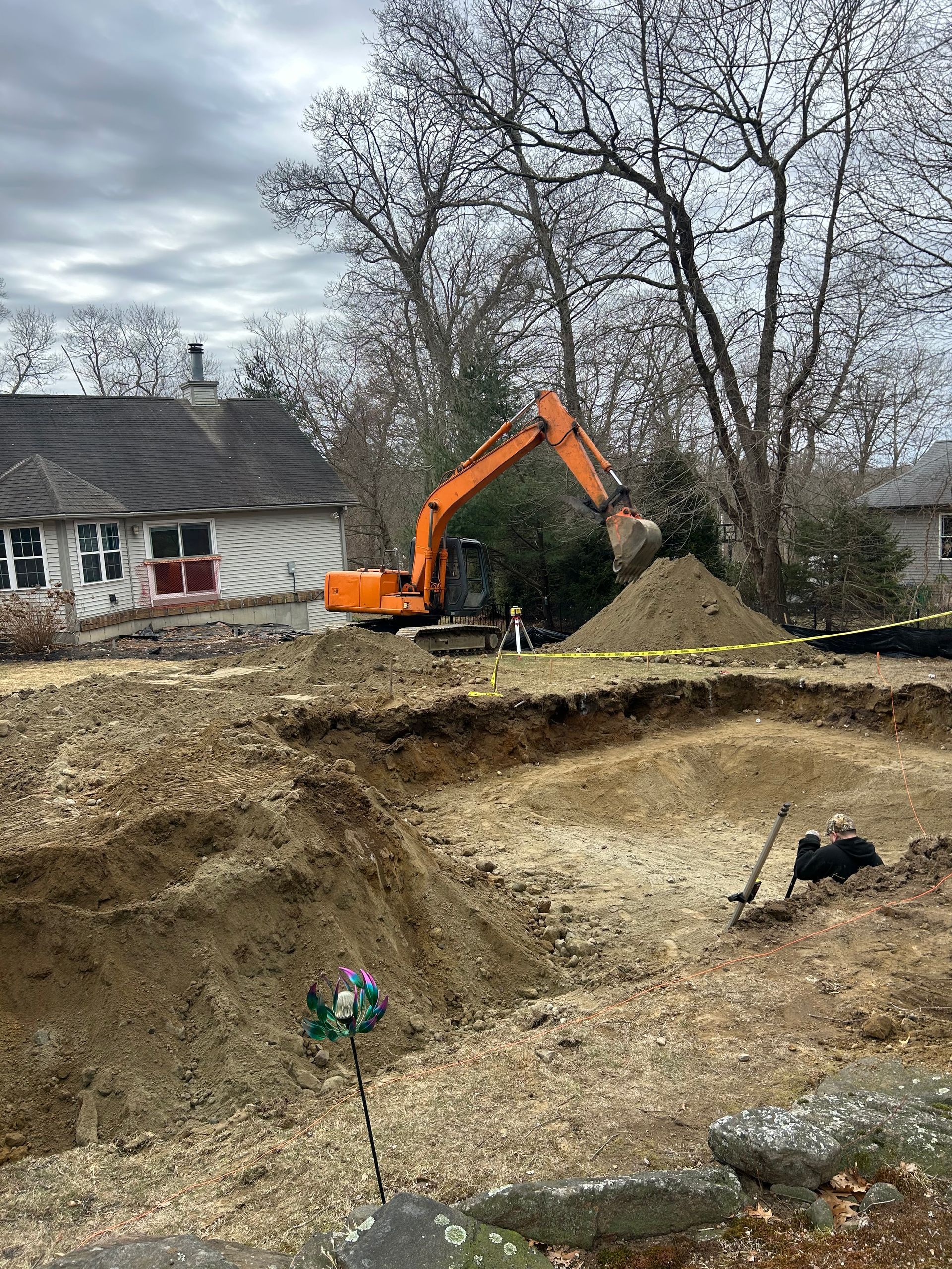 An excavator is digging a hole in the dirt in front of a house.