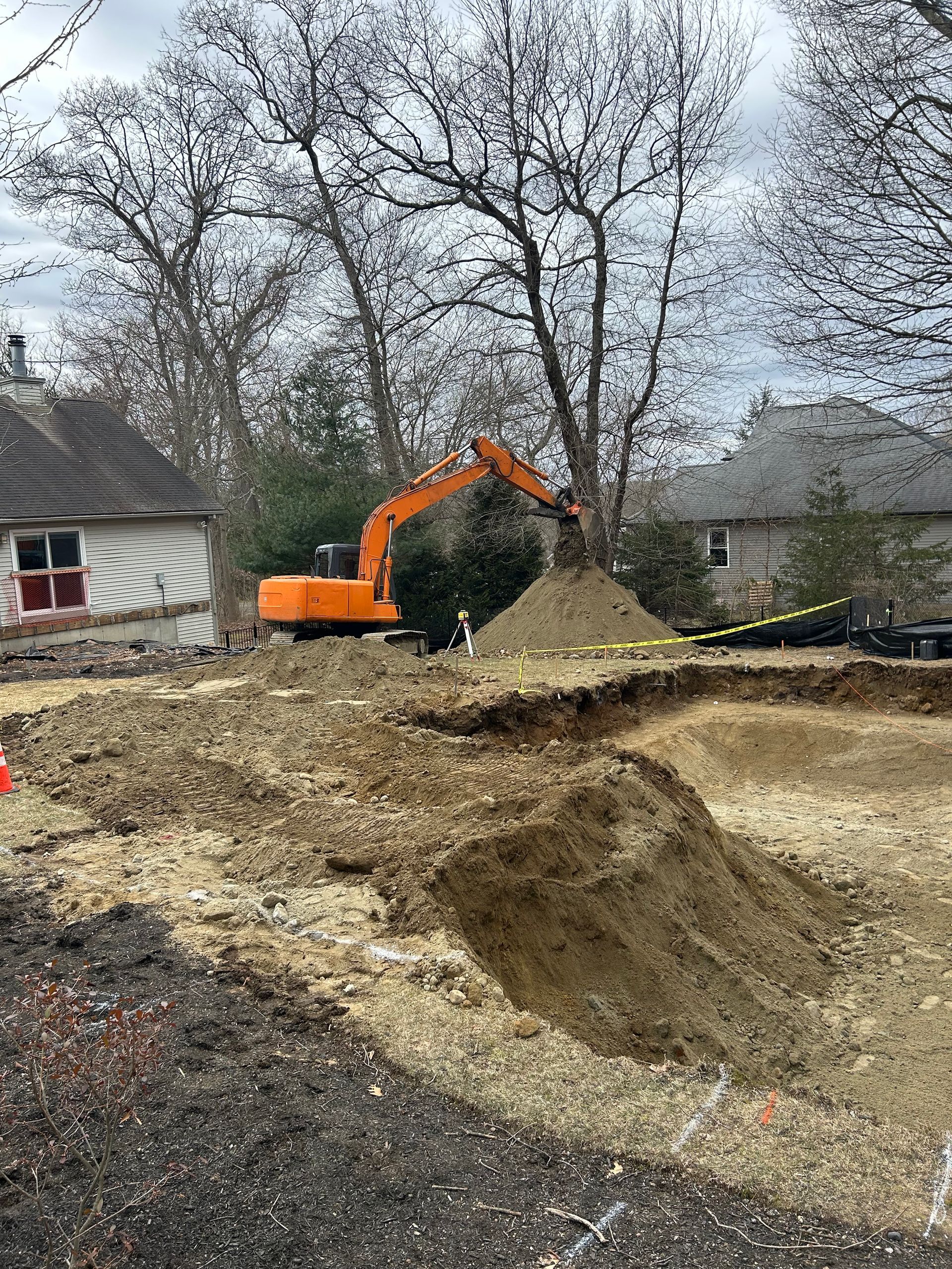 A large orange excavator is digging a hole in the dirt in front of a house.