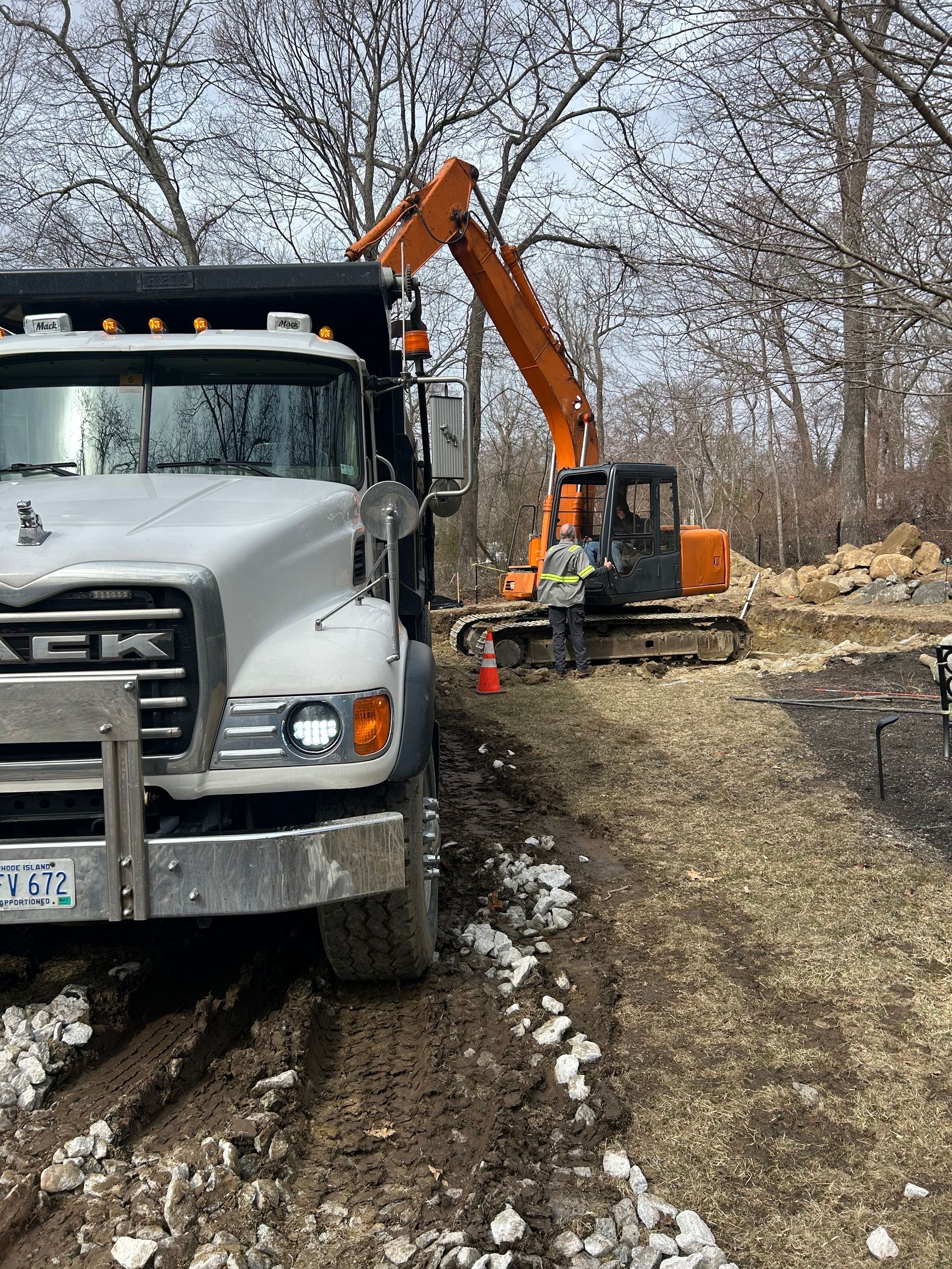 A dump truck is driving down a dirt road next to an excavator.