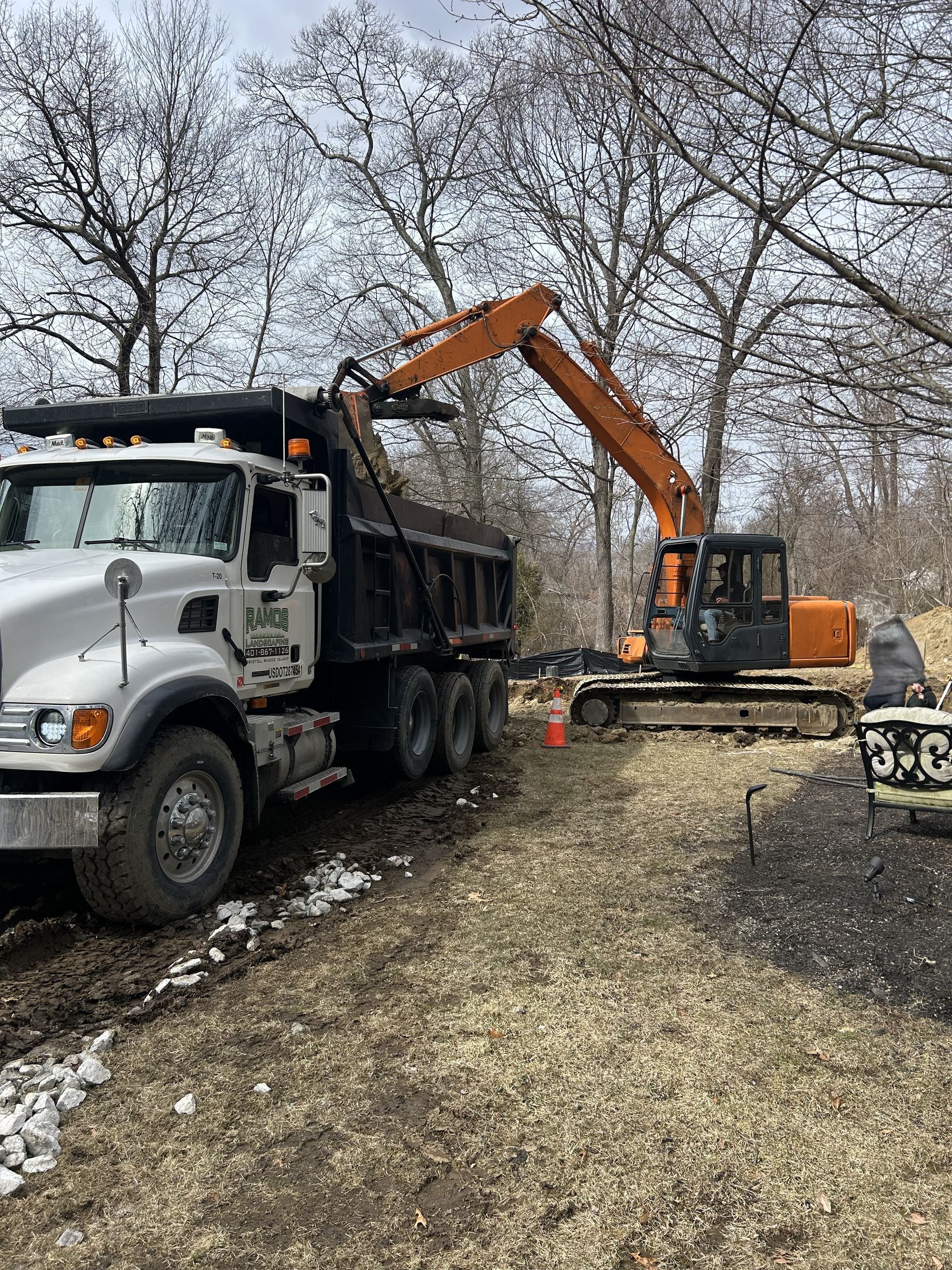 A dump truck is parked in a dirt lot next to an excavator.