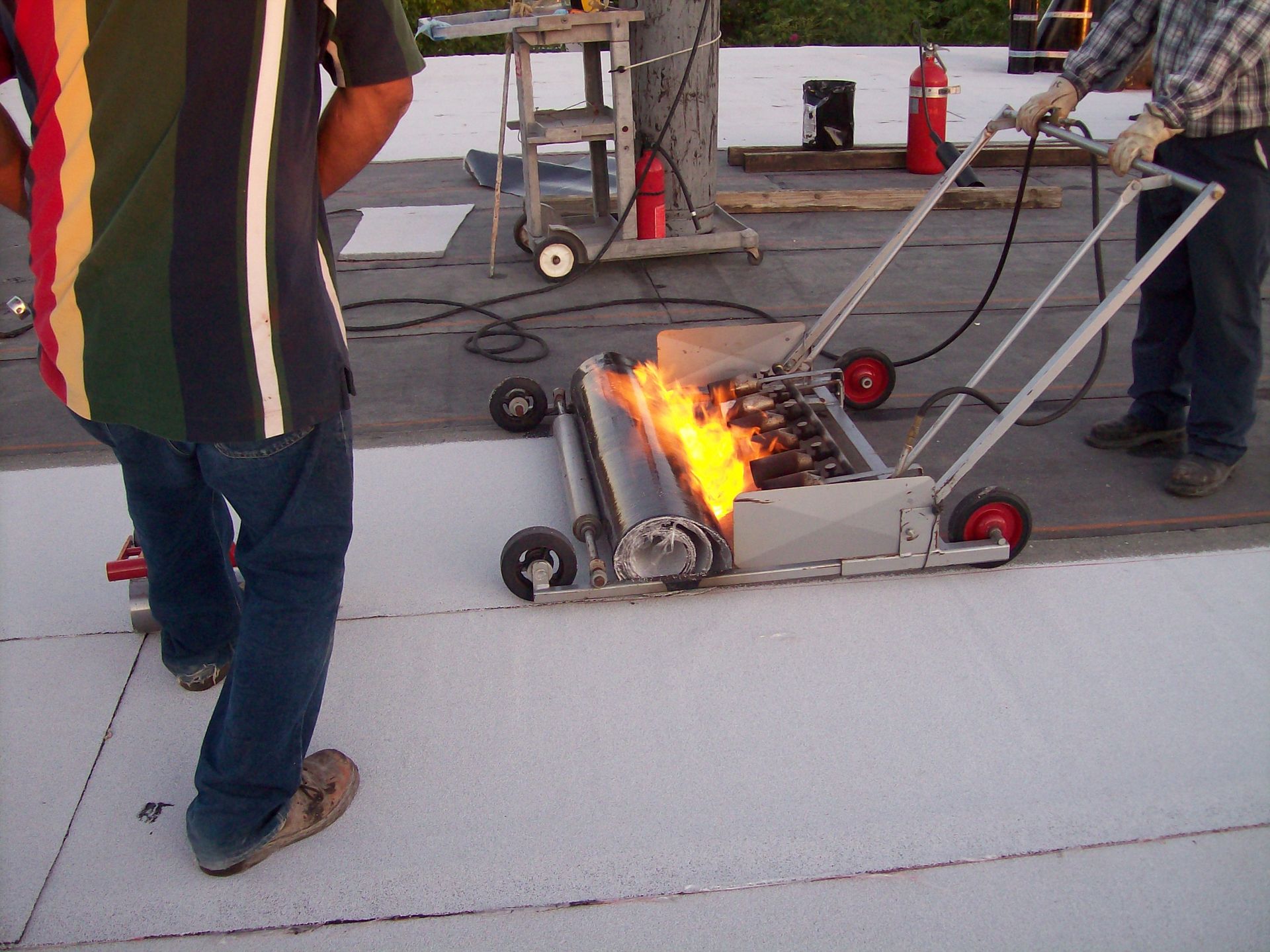 Two men are working on a roof with a fire extinguisher in the background