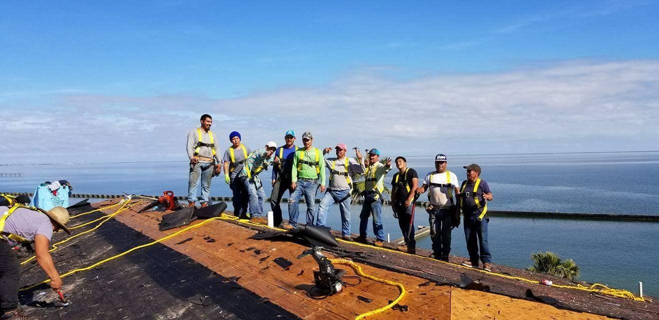 A group of construction workers are standing on top of a roof overlooking the ocean.