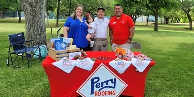 A group of people standing around a perry roofing table in a park.