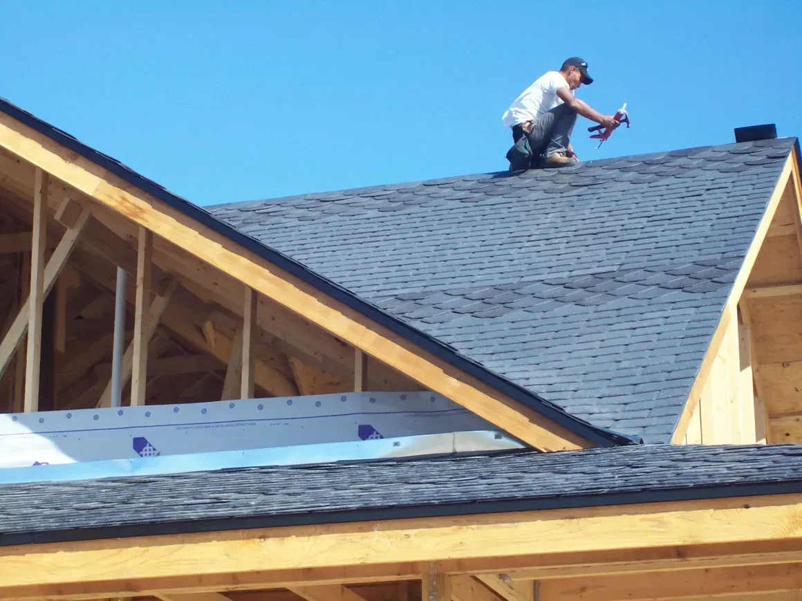 A man is working on the roof of a house under construction