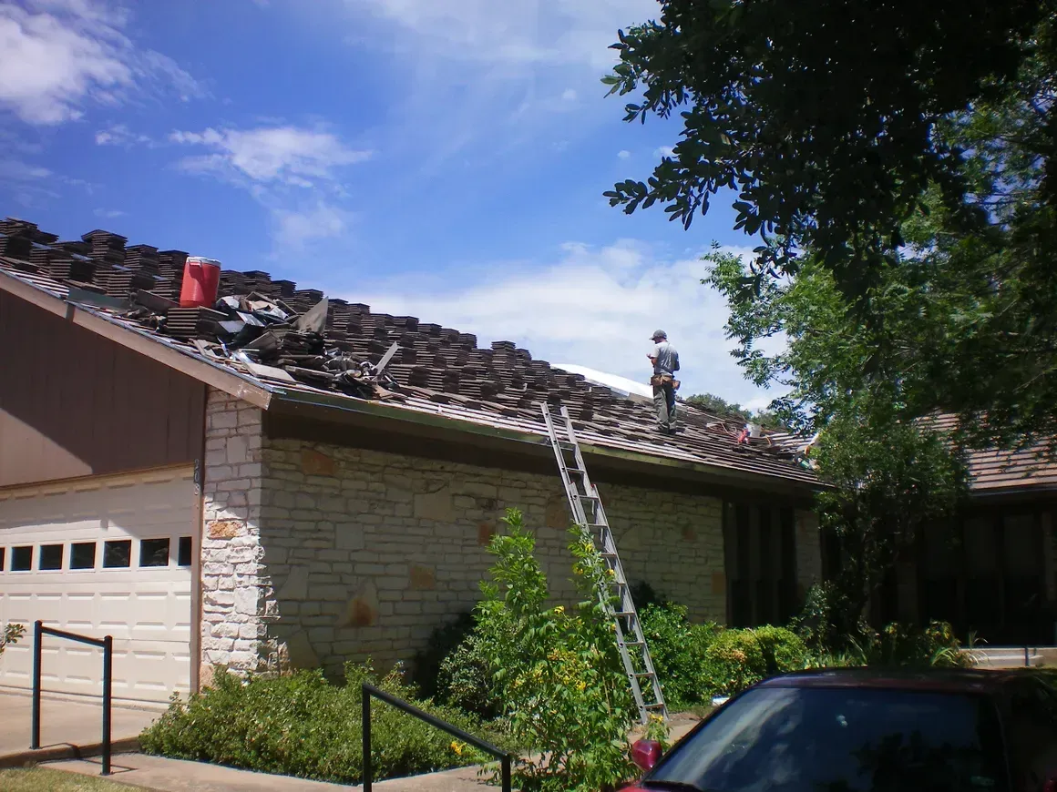 A man on a ladder is working on the roof of a house
