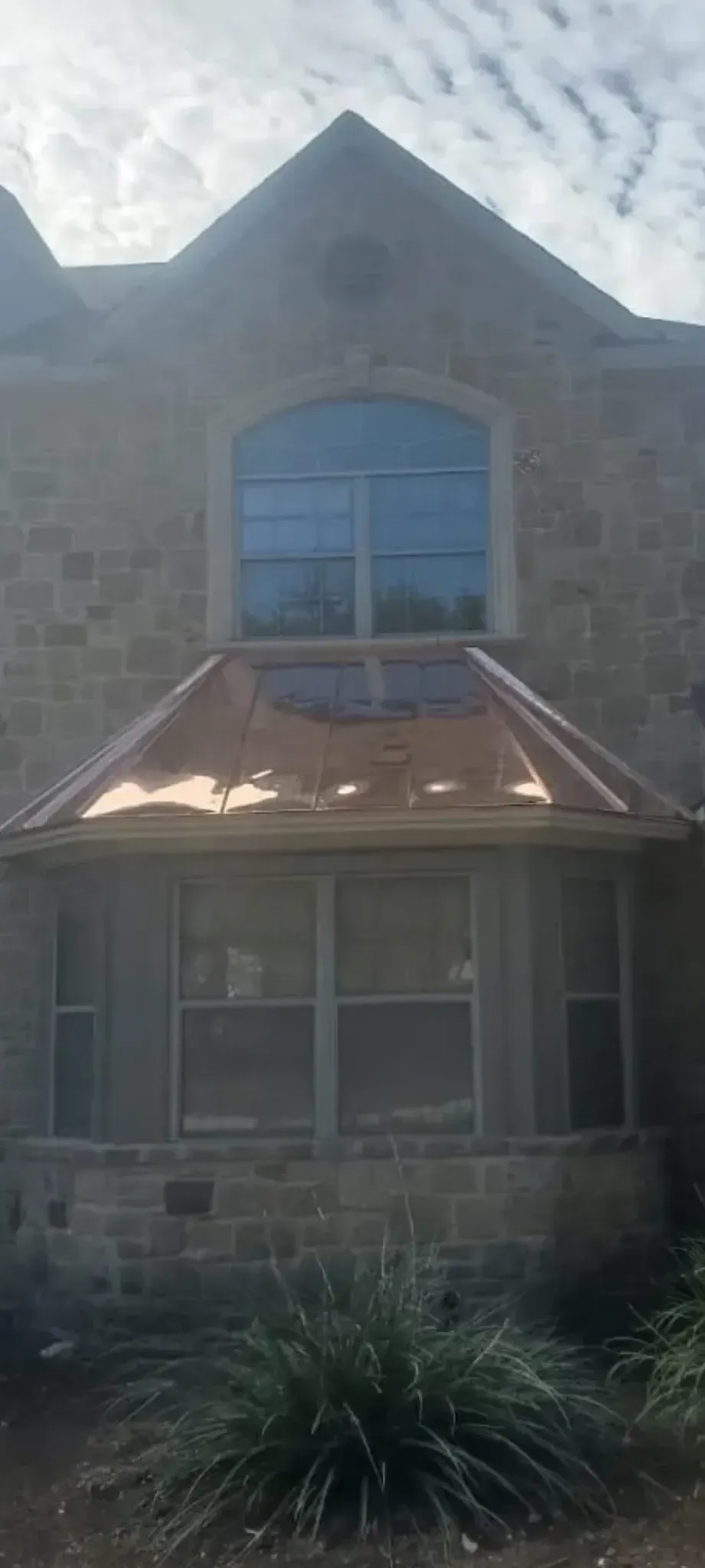A large brick house with a large window and a copper roof.