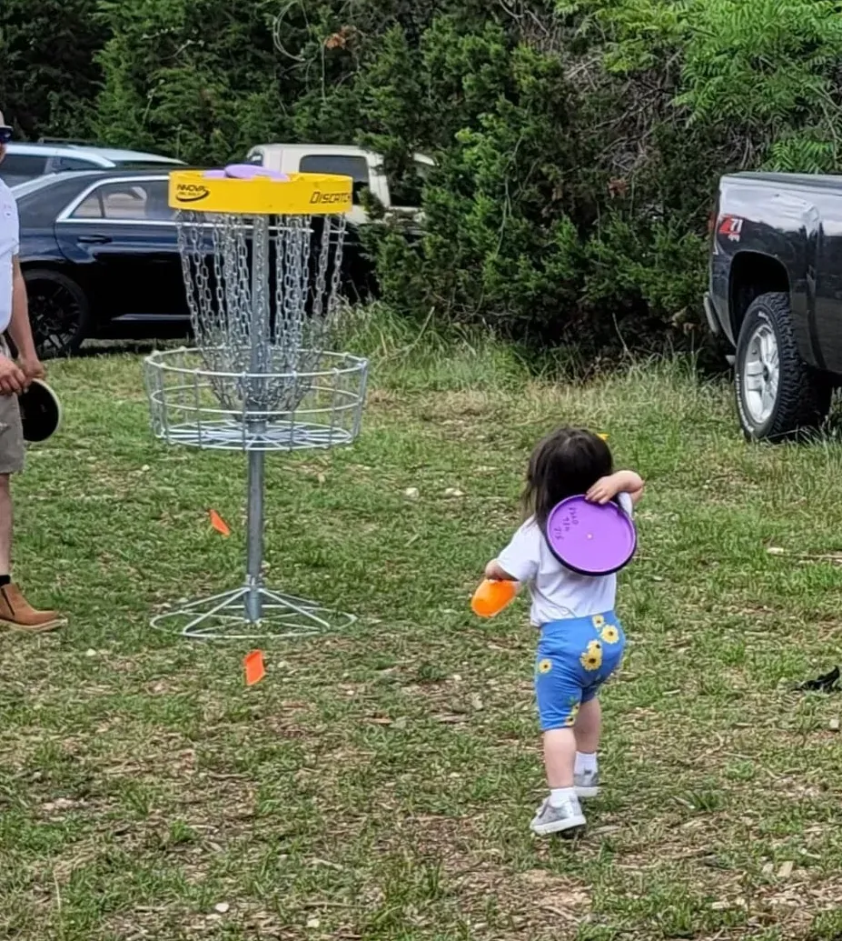 A little girl is throwing a frisbee at a frisbee golf course.