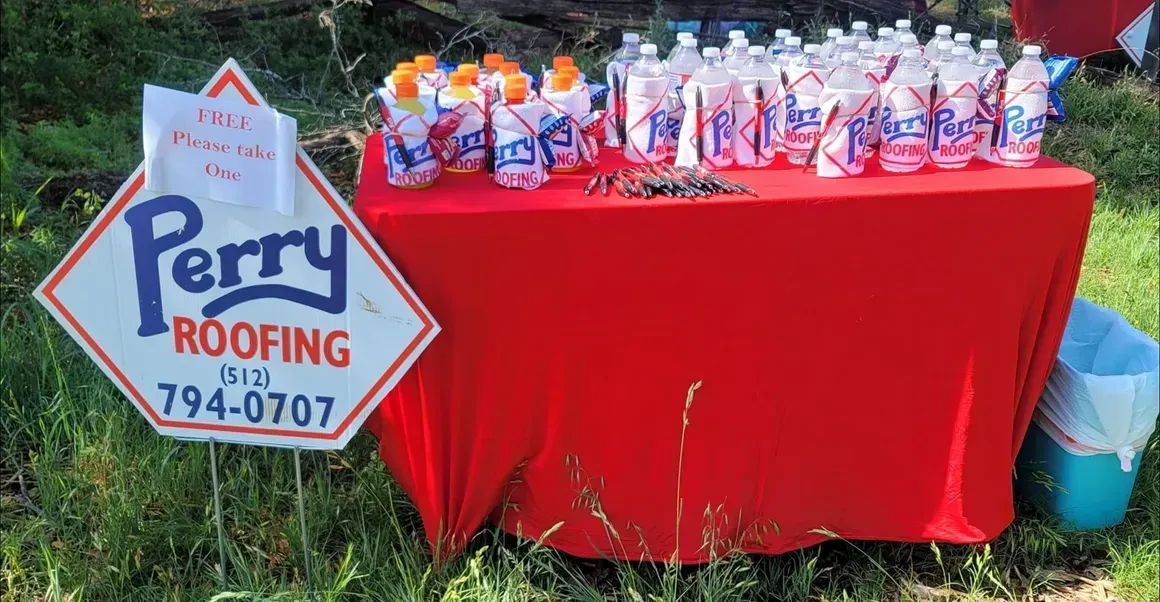A perry roofing sign is next to a table with water bottles on it.