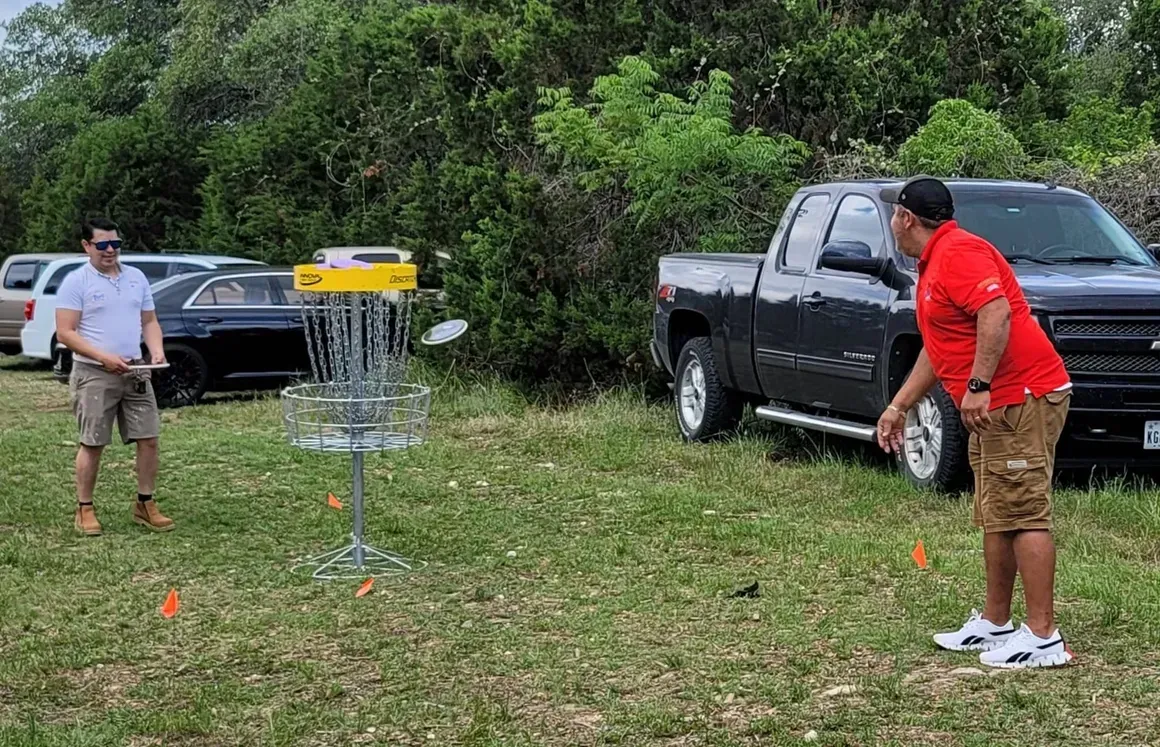 Two men are playing frisbee golf in a field next to a truck.