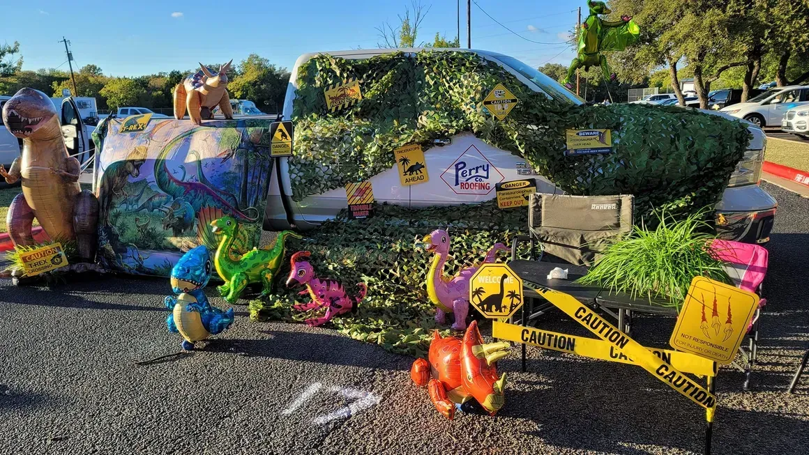 A truck is decorated with dinosaurs and balloons and is sitting on the side of the road.