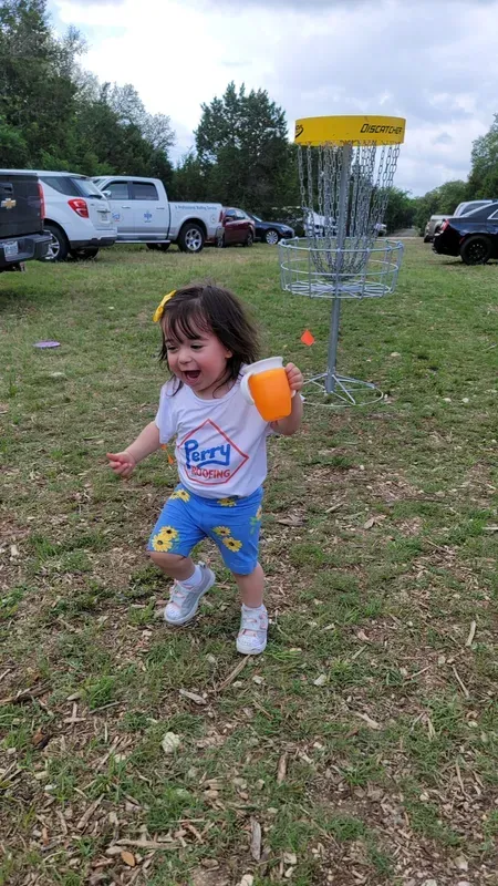 A little girl is playing frisbee golf in a park.