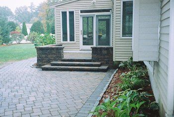 Brick walkway leading to a house entrance with steps and a small retaining wall. Landscaping on the right.
