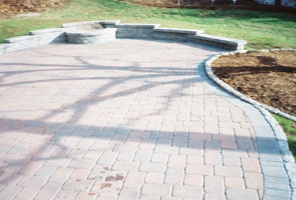 Brick patio with curved walkway, stone retaining wall, and green grass.