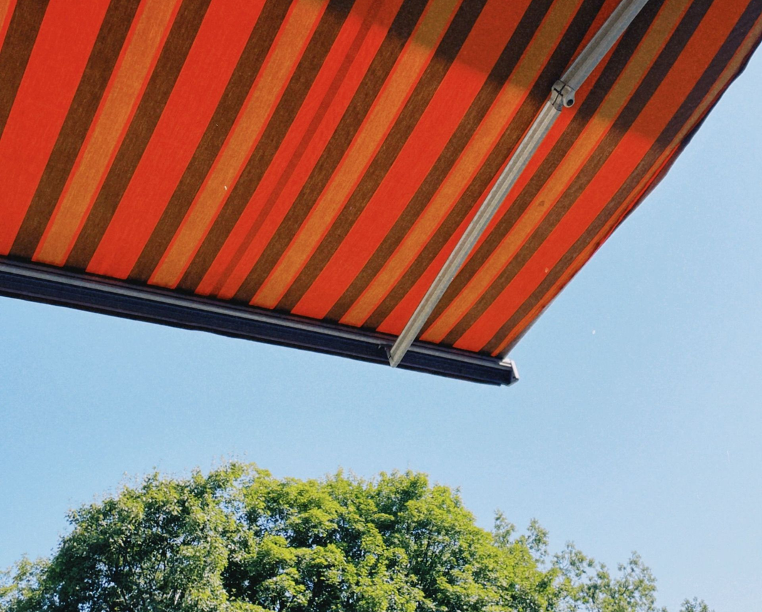 Striped orange awning over blue sky with treetops below