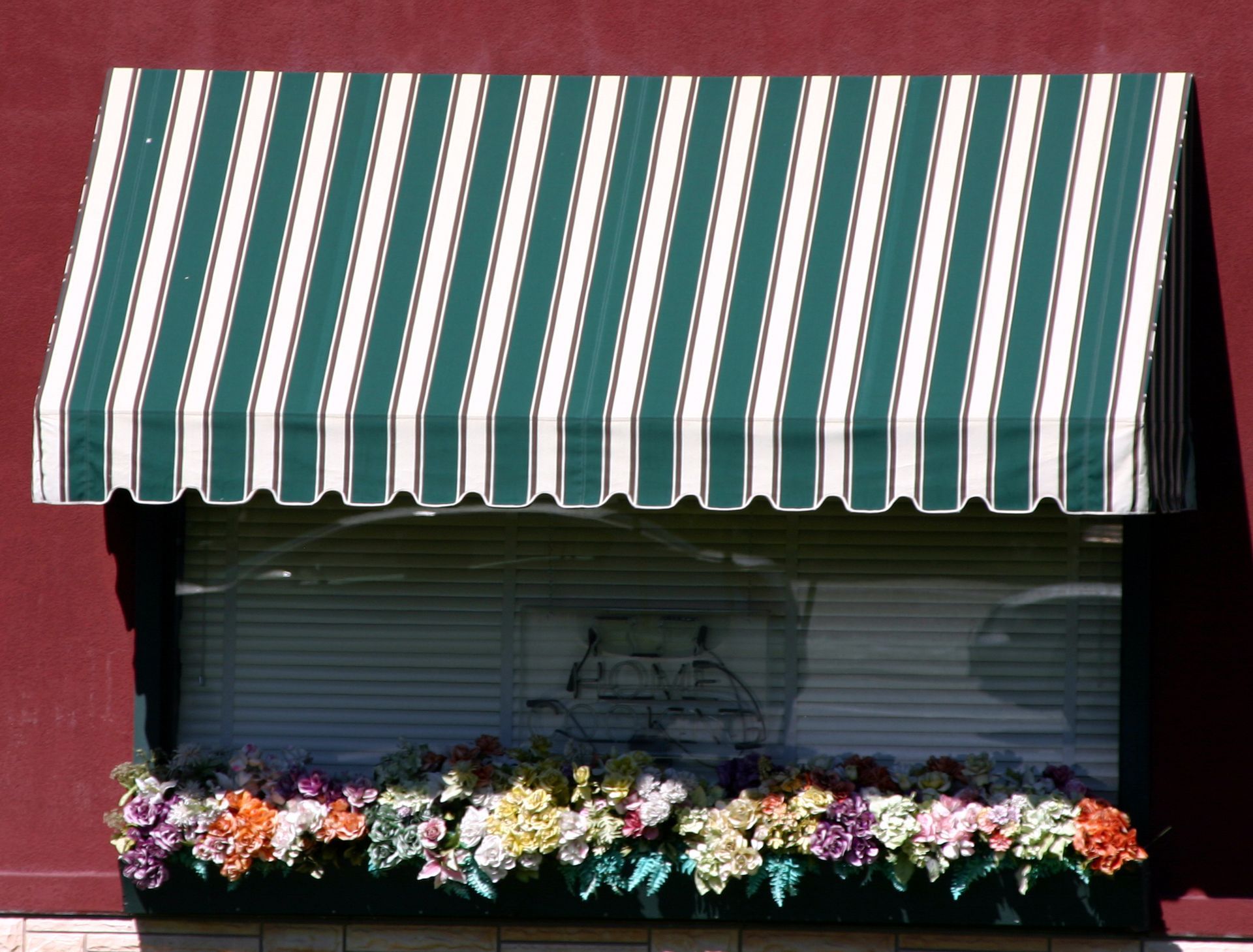 Closed storefront with a green-and-white striped awning and flower boxes against a red wall