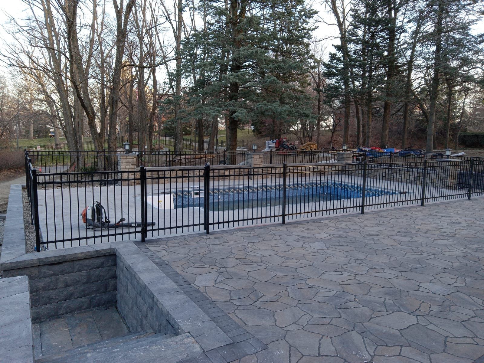 A fence surrounds a swimming pool with trees in the background