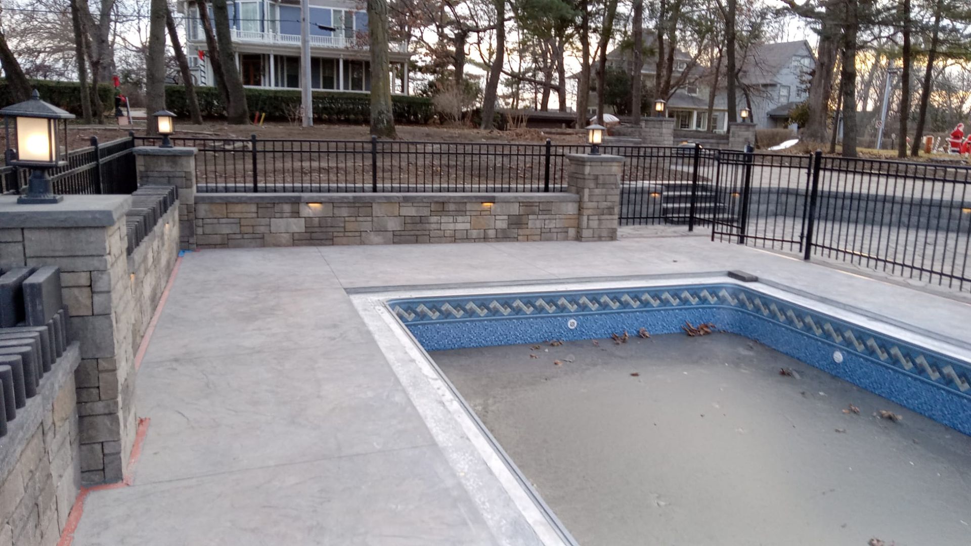 An empty swimming pool with a fence around it and a house in the background