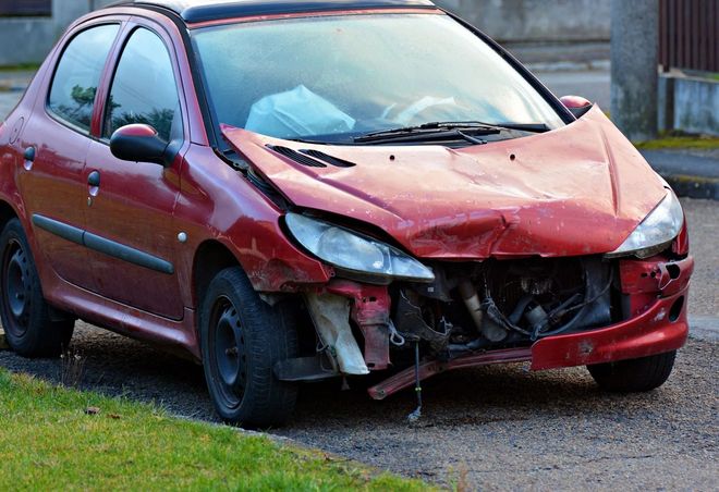 Damaged red car with a crumpled front end parked on grass