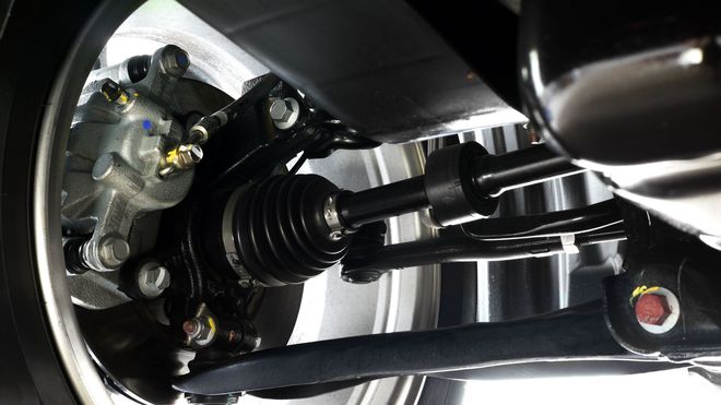 Close-up of a car wheel hub and suspension assembly with black metal arms and a rubber CV boot