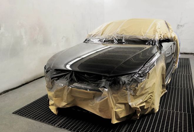 Black car in a spray booth, masked with plastic and paper, ready for painting