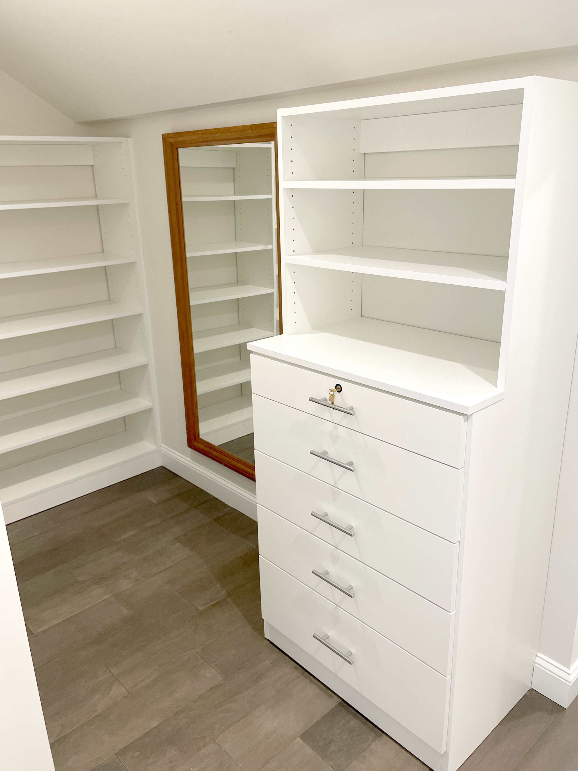 A walk-in closet with a dresser, shelves, and a mirror.