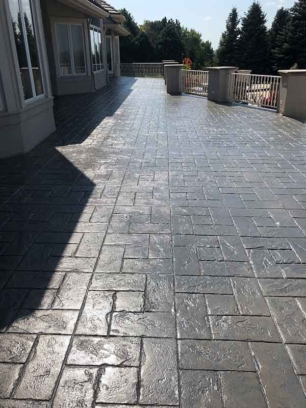 A large brick patio with a railing and trees in the background.