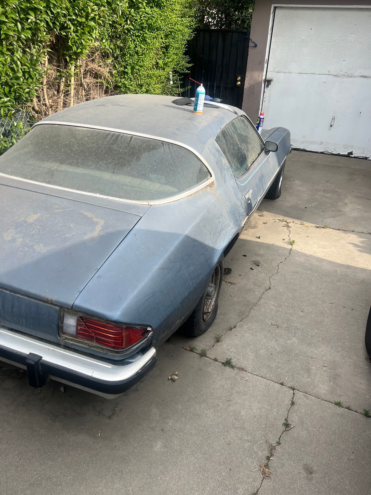 An old car is parked in a driveway next to a garage door.