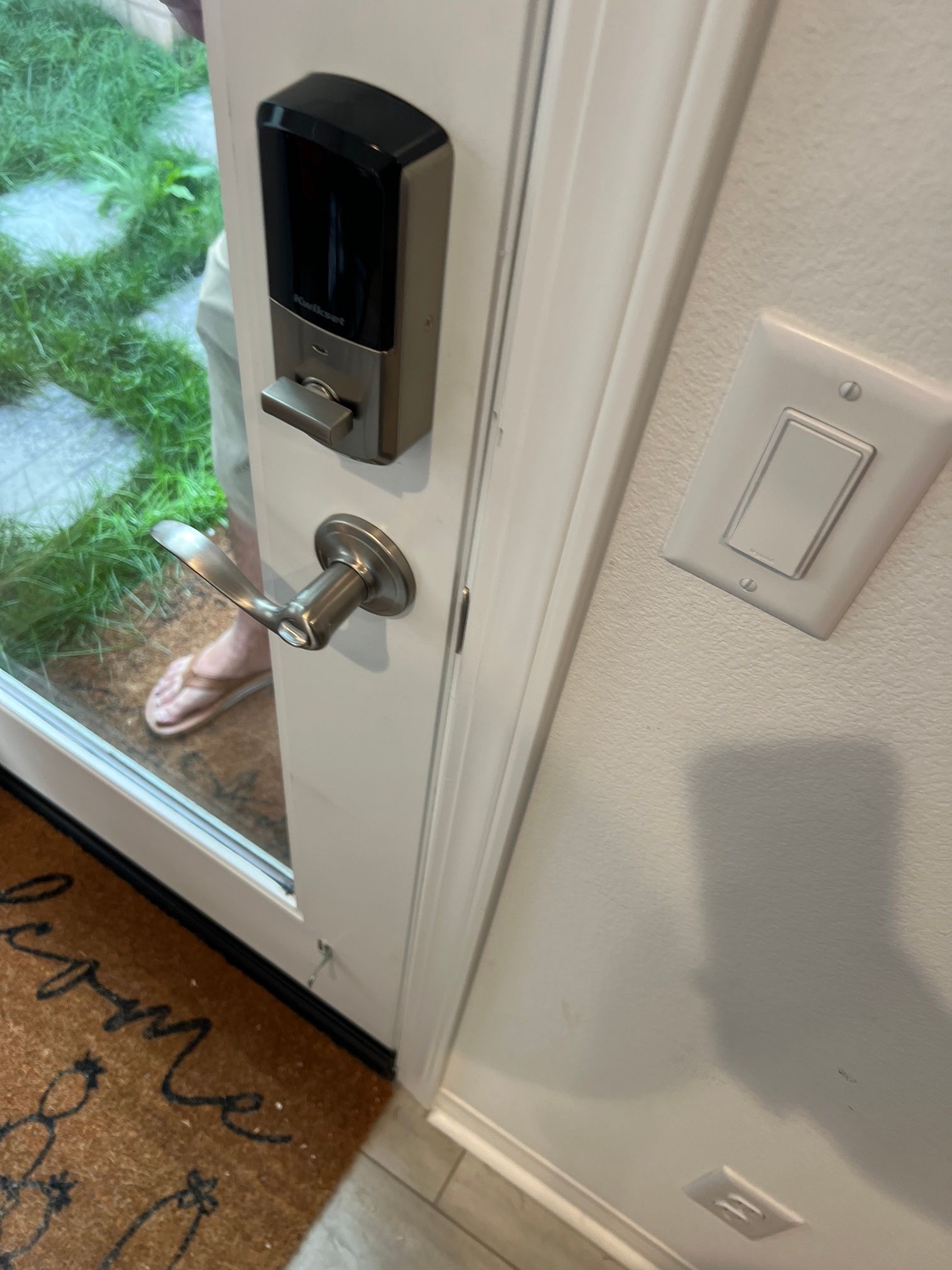 A person is standing in front of a door with a door lock and a light switch.