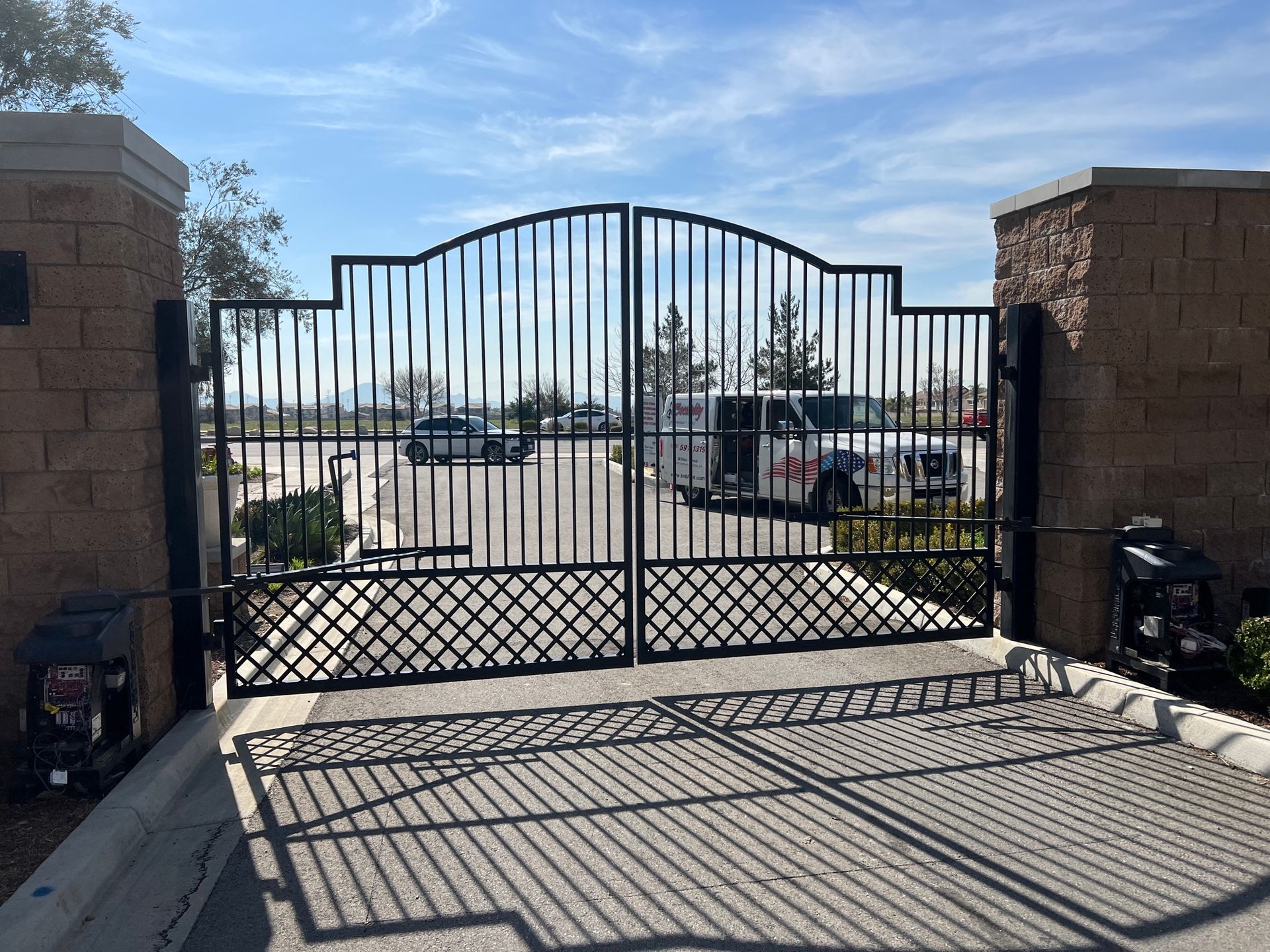 A wrought iron gate is open to a parking lot.