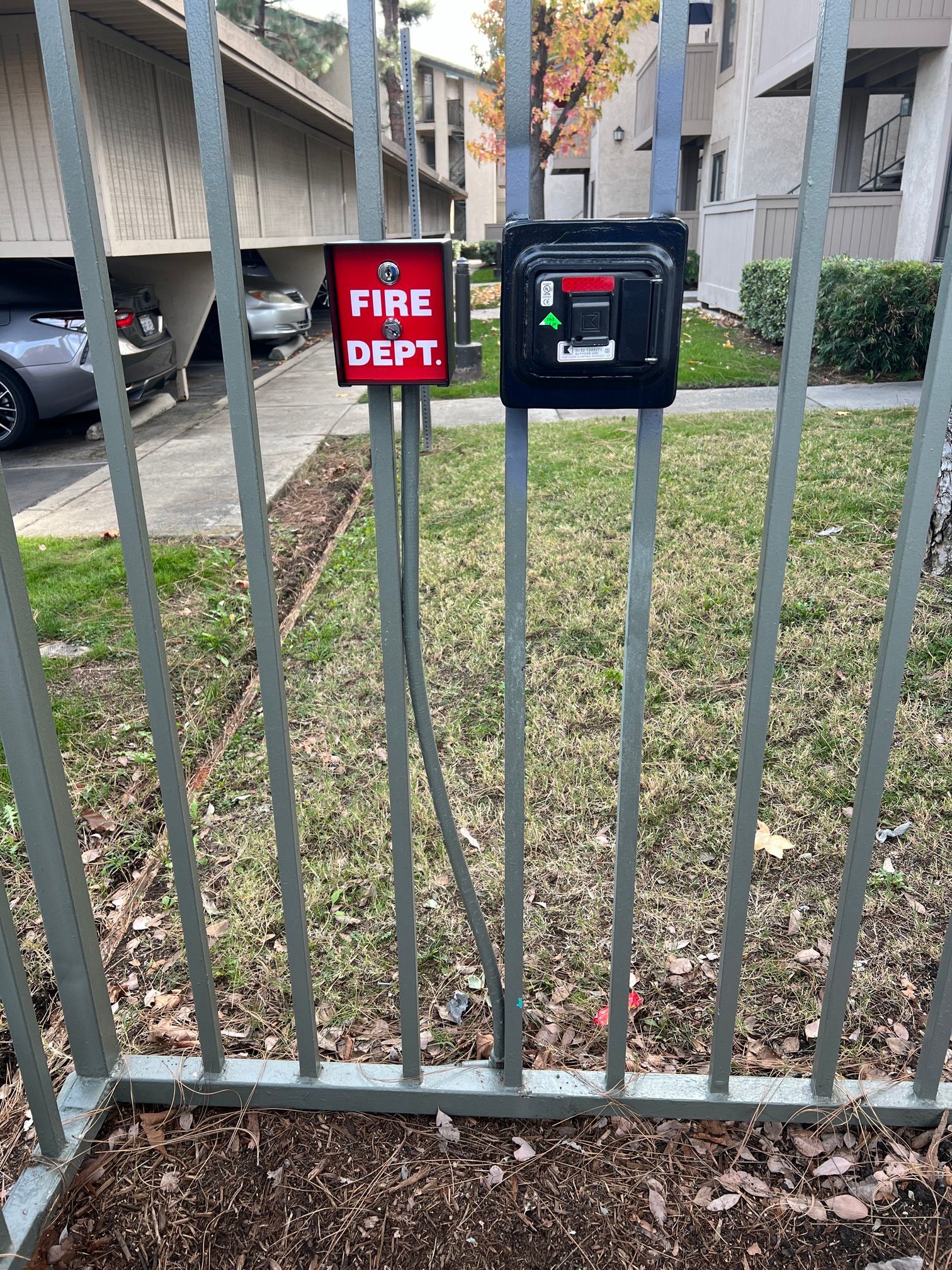 A fire alarm is sitting on top of a metal fence.