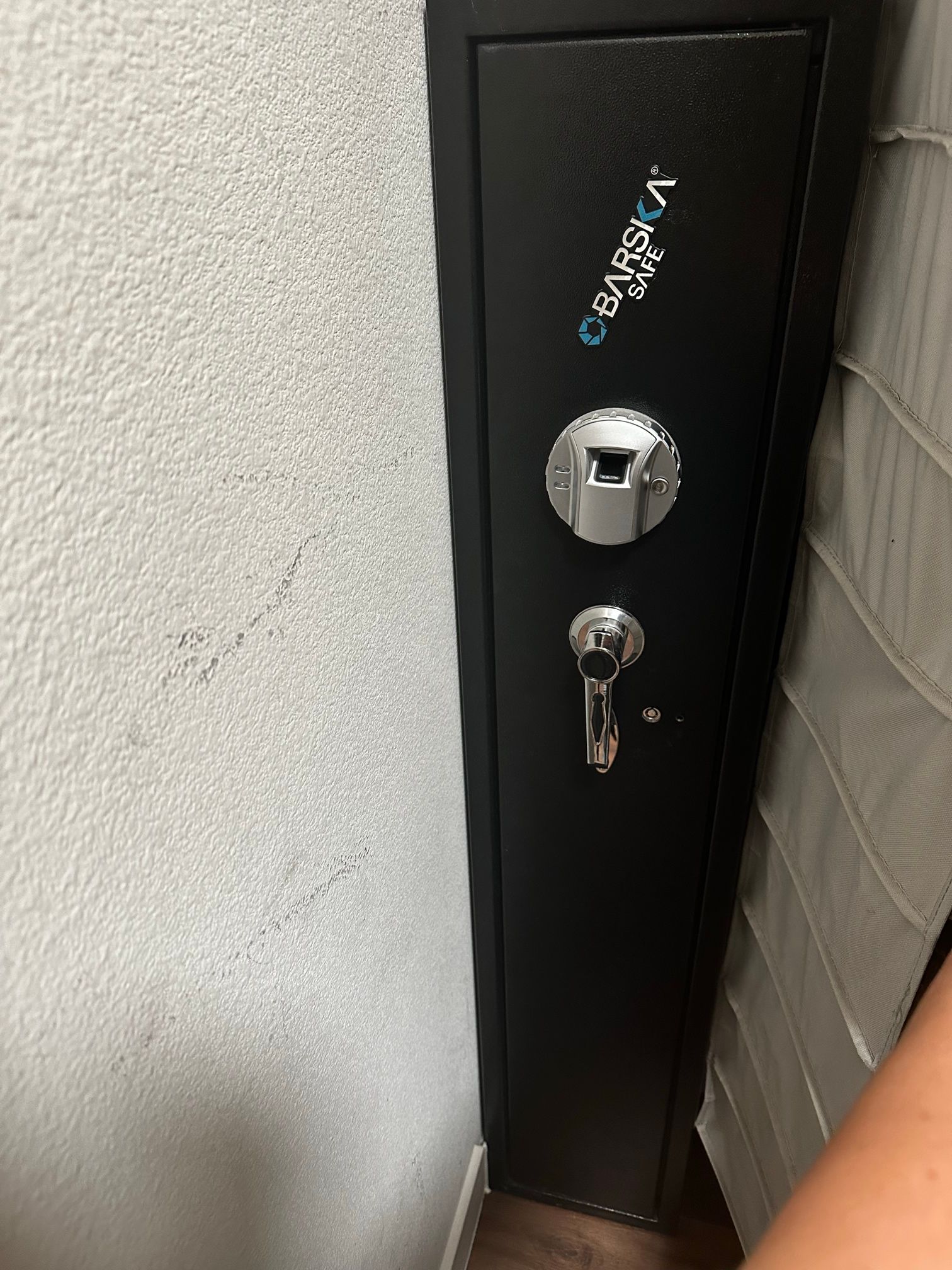 A person is standing next to a black safe with a fingerprint lock.