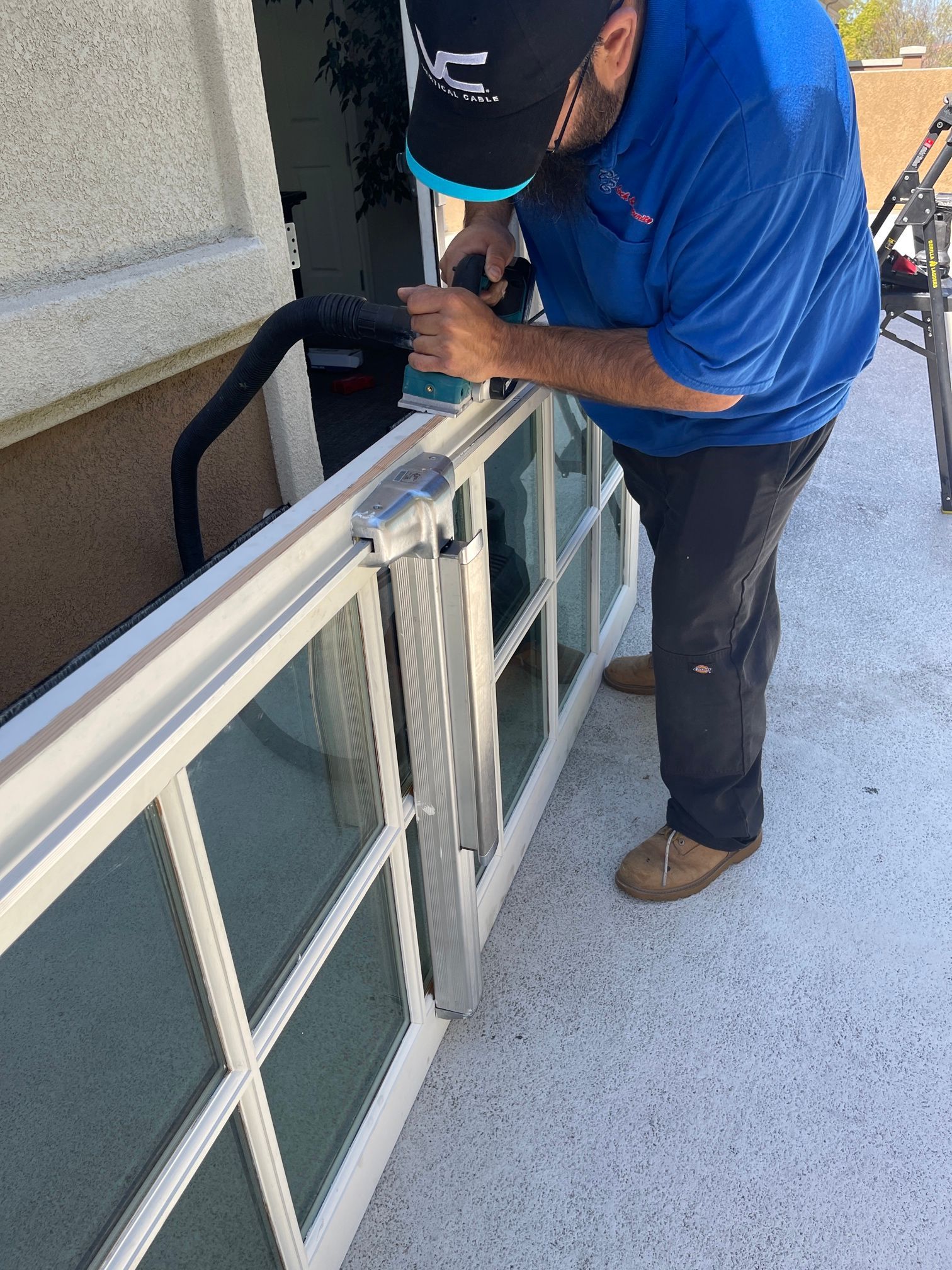 A man in a blue shirt is sanding a window with a sander.
