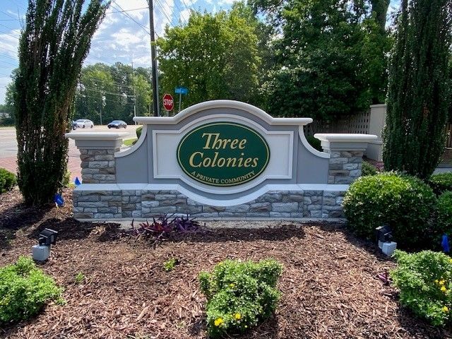 A sign for three colonies is surrounded by bushes and trees