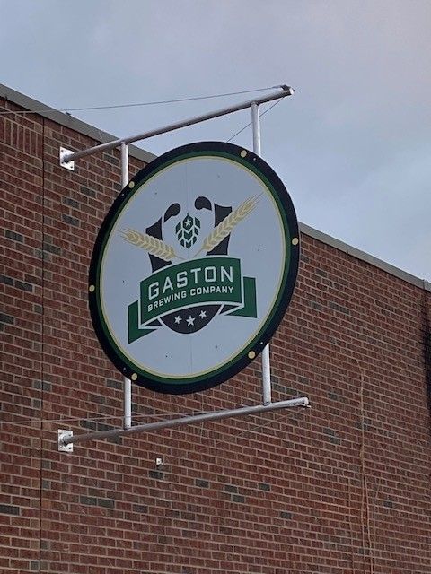 A gaston brewing company sign hangs from the side of a brick building