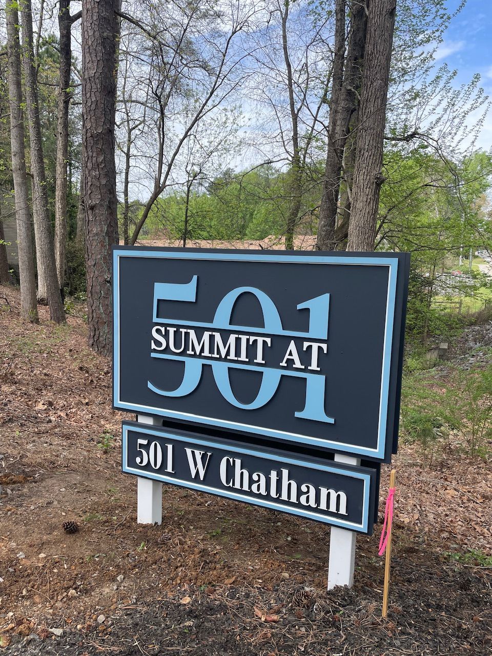 A sign for summit at 501 w chatham is sitting in the middle of a forest.