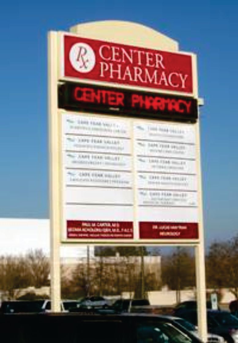 A sign for the center pharmacy with cars parked in front of it