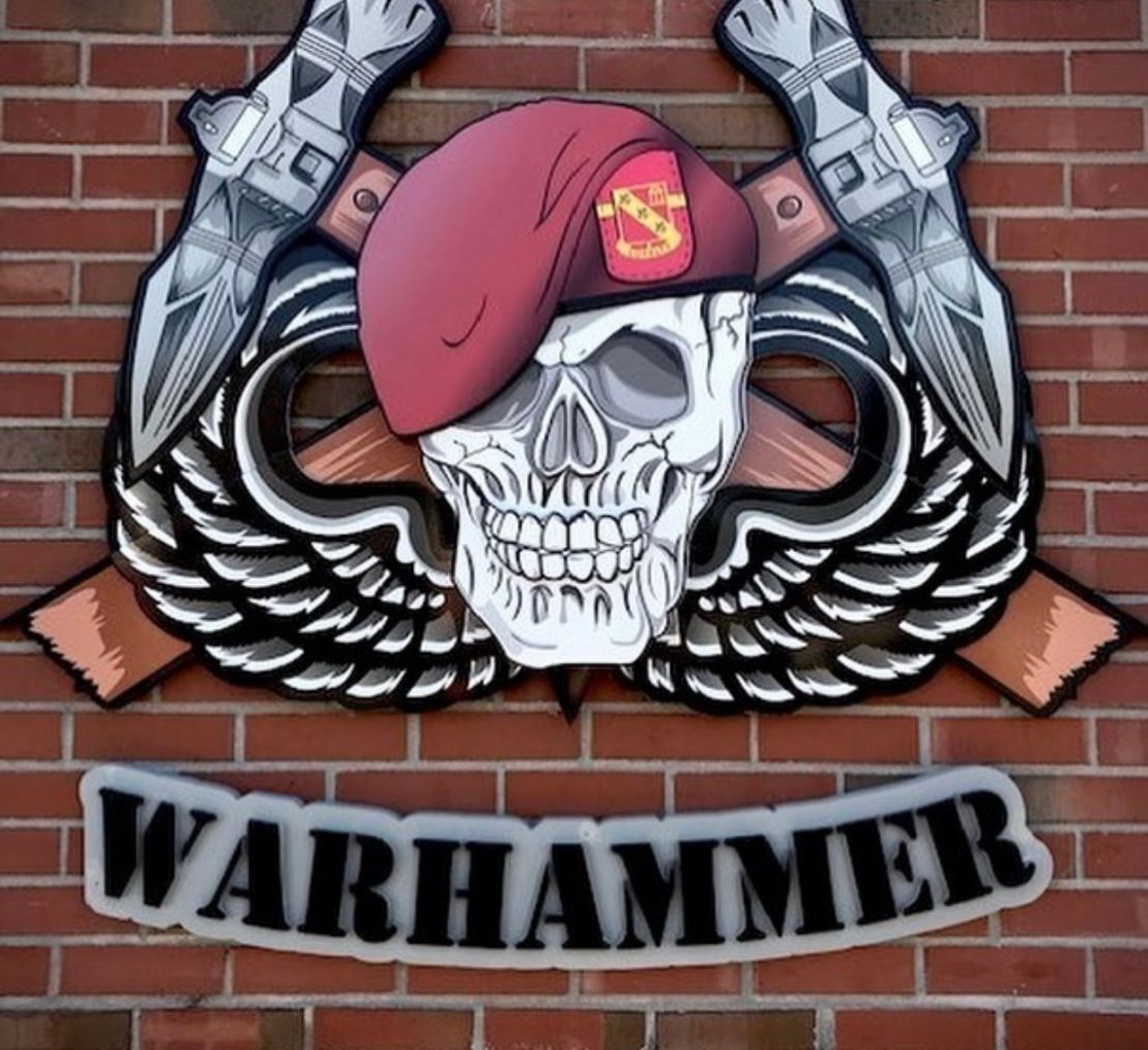 A warhammer logo with a skull wearing a red beret