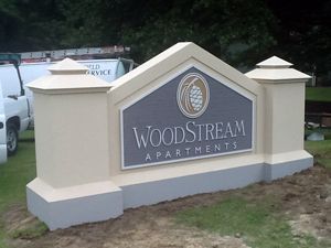 A sign for woodstream apartments is sitting in the grass