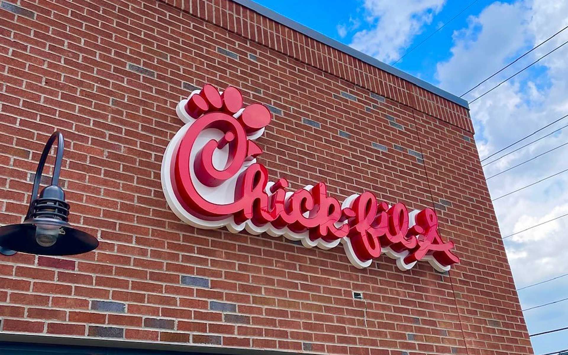 A chick-fil-a sign is on the side of a brick building.