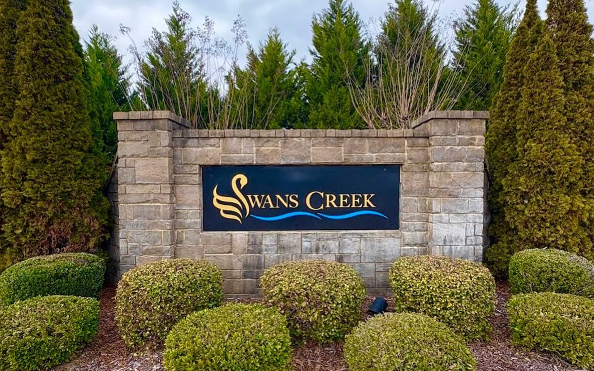 A sign for swans creek is surrounded by bushes and trees