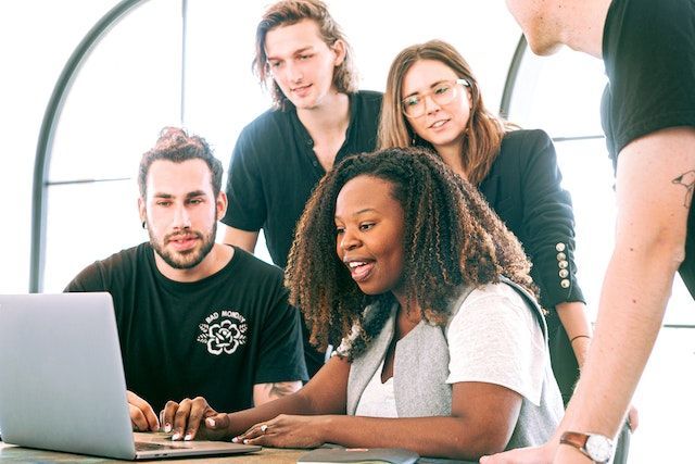 4 people watch as their manager instructs them on her laptop