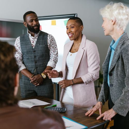 A Black woman in a pink blazer addresses a small team